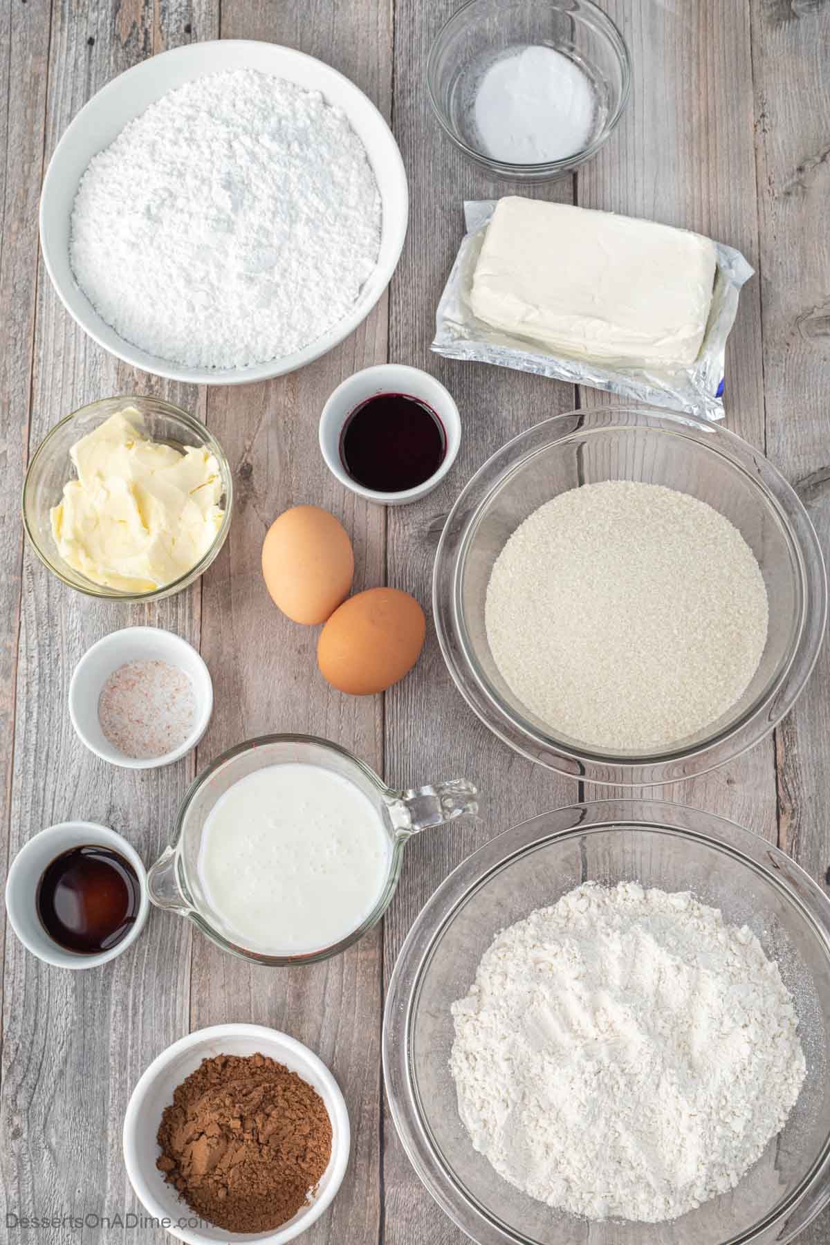 White Chocolate Pumpkin Spice Latte Recipe 4 The image shows a flat layout of baking ingredients arranged neatly on a white marbled surface. Starting from the top left, there is a large white bowl filled with white powdered sugar, next to it a small clear bowl with white baking soda, and a block of cream cheese in silver foil. Below those, on the right, there is a large clear bowl filled with granulated white sugar and another clear large bowl filled with white flour sits at the bottom right. Moving left to right in the middle row, there’s a small white bowl with dark brown liquid, two brown eggs, a small white bowl with pink salt, and a small white bowl with dark vanilla extract. Towards the bottom left, there is a clear glass jug filled with white milk or cream, a small glass bowl with pale yellow softened butter, and a small white bowl of cocoa powder at the bottom. The ingredients are organized in layers of bowls and containers with different textures and colors, all placed on a rustic wood-patterned surface. photo taken with an iphone --ar 4:5 --v 7