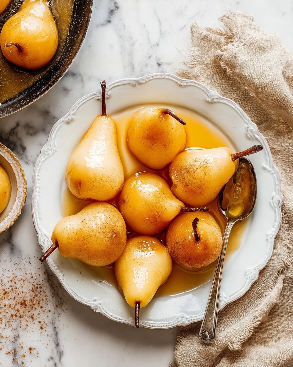 The image shows a round white plate with a scalloped edge filled with seven poached pears, each a light golden color with a smooth texture, gently shiny from syrup and sprinkled with cinnamon. The pears are arranged casually, some with their stems still attached, and have small pools of caramel-colored syrup in their hollow tops. On the right side of the plate, a vintage silver spoon is resting under one pear. To the left, a skillet with more pears in syrup is partly visible on a white marbled surface, along with a beige linen cloth near the bottom right. Photo taken with an iphone --ar 4:5 --v 7