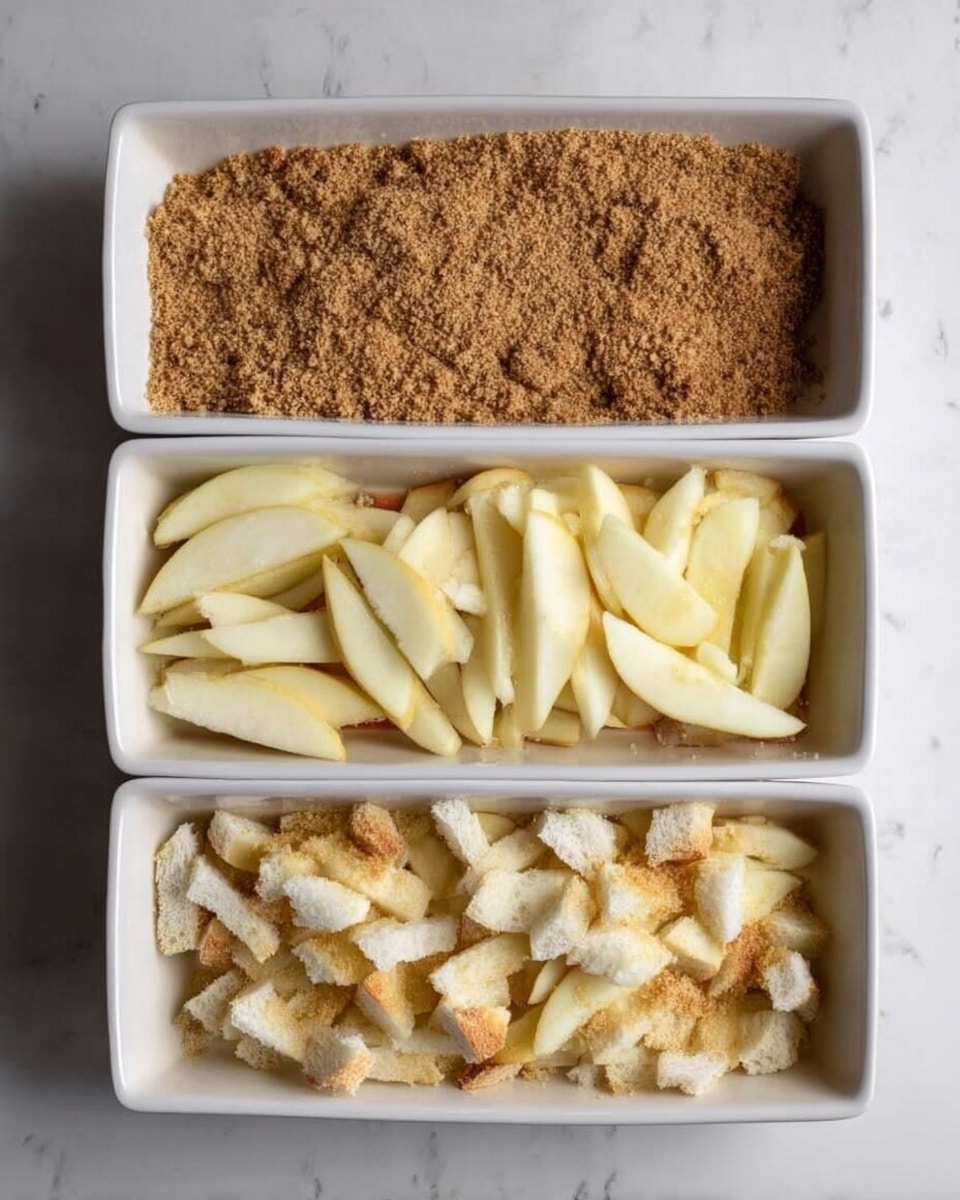 A white rectangular dish sits on a white marbled surface, shown in three stages of layering. In the first stage, the dish is evenly covered with a layer of light brown crumbs with a coarse texture. The second stage adds a layer of sliced pale yellow apples arranged loosely over the crumb base, the slices showing smooth, slightly shiny surfaces. The third stage adds an uneven layer of roughly torn white bread pieces with some golden crust bits scattered over the apple slices, filling the dish almost to the top. Photo taken with an iphone --ar 4:5 --v 7