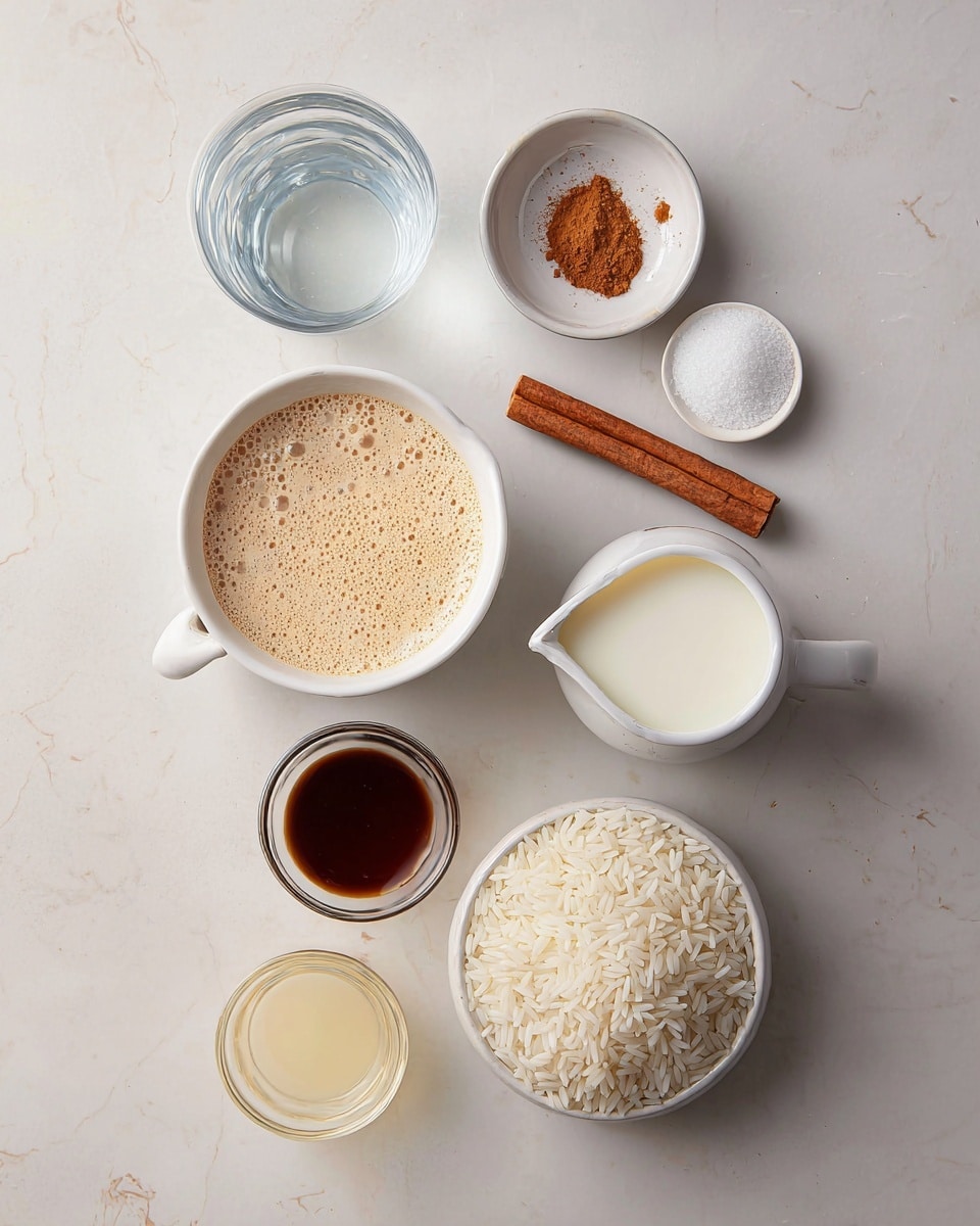 The image shows several ingredients laid out on a white marbled surface, arranged neatly. There is a white bowl filled with uncooked white rice positioned to the right, and next to it is a small white cup with granulated white sugar. Above these, there is a cinnamon stick placed horizontally. Near the center is a white pitcher filled with a creamy beige liquid, likely a spiced milk mixture, with foam bubbles on its surface. To the left of it, there is a small bowl with ground cinnamon and another small bowl with a dark brown syrup or extract. Below these, a transparent glass container holds white milk, and next to it is a small glass filled with a pale yellow liquid, likely condensed milk. At the top center, a clear glass holds water. The whole setup looks clean and simple. Photo taken with an iphone --ar 4:5 --v 7