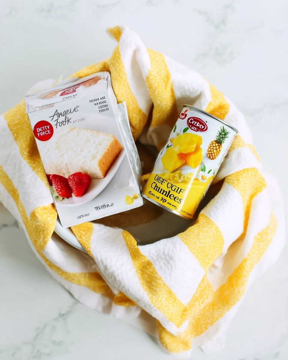 A white bowl holds a yellow and white striped cloth with soft folds. Inside the cloth, there is a box of Betty Crocker Angel Food Cake Mix, showing a picture of a white fluffy cake slice with a golden brown edge and red strawberries on a white plate. Next to the box, a can of Great Value Pineapple Chunks sits, featuring images of bright yellow pineapple pieces and a pineapple slice on its label. The bowl is set on a white marbled surface. photo taken with an iphone --ar 4:5 --v 7