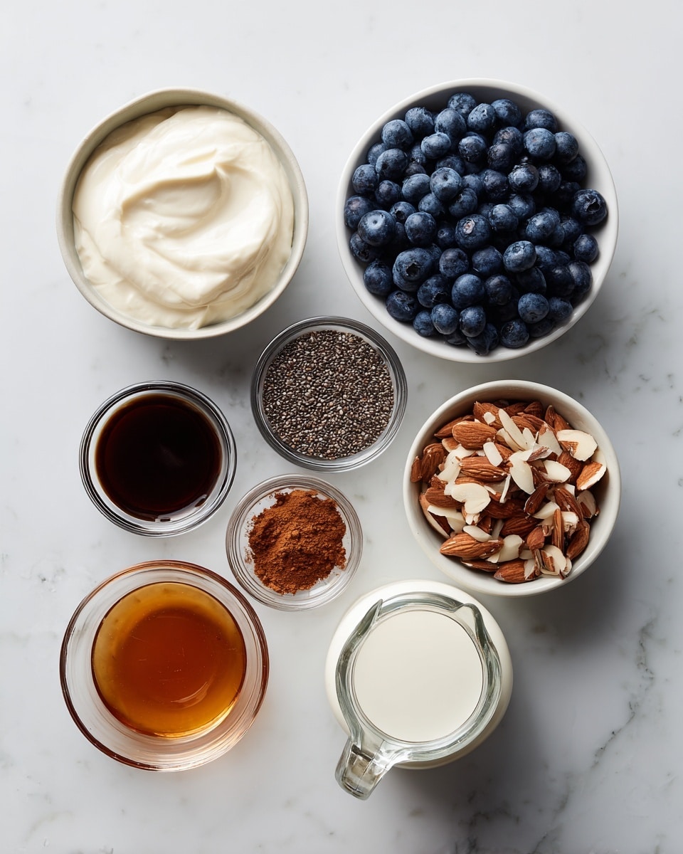 The image shows seven small bowls and a glass jug arranged on a white marbled surface. The top middle bowl contains smooth, creamy white yogurt. To its right, a white bowl is filled with fresh, plump blueberries that have a deep blue color. Below the yogurt, a bowl holds roughly chopped almonds showing white and brown textures mixed together. Next to it on the right, another bowl contains a fine, brown powder of cinnamon. On the left side below the yogurt, a white bowl is filled with tiny, dark chia seeds. Above chia seeds on the left is a small glass bowl filled with dark brown vanilla extract. Below that, another small glass bowl contains amber-colored maple syrup with a clear surface shine. In the center bottom is a transparent glass jug filled with white milk. All items are placed neatly with consistent spacing on the smooth white marbled background. Photo taken with an iphone --ar 4:5 --v 7