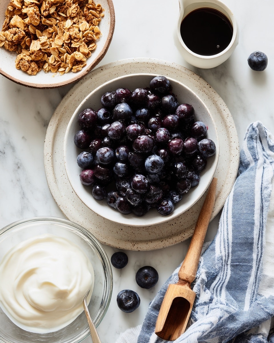 The image shows a clean white bowl filled with dark purple frozen blueberries on a light speckled round plate, placed on a white marbled surface. To the top right is a small white cup filled with dark syrup. Below and to the right is another white bowl, filled with golden brown granola and a small wooden scoop resting on top. At the bottom left, there is a glass bowl of thick, smooth white yogurt. Next to the bowls, a blue and white striped cloth is casually placed on the surface. Photo taken with an iphone --ar 4:5 --v 7