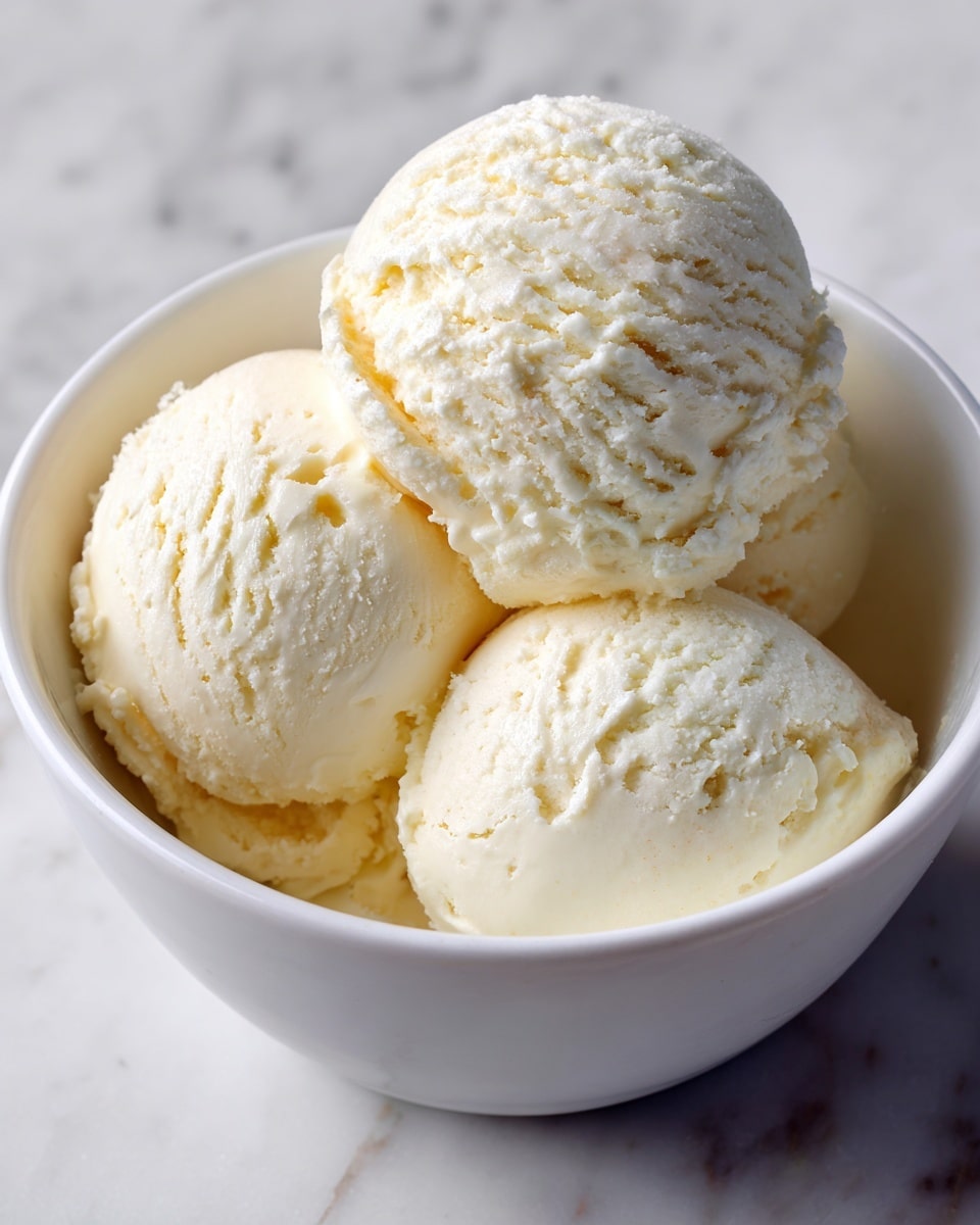 A white bowl with small black specks holds three round scoops of creamy white ice cream closely placed next to each other. The ice cream has a smooth and soft texture with small uneven edges that show slight melting. The bowl sits on a white marbled surface, providing a clean and simple background. Photo taken with an iphone --ar 4:5 --v 7