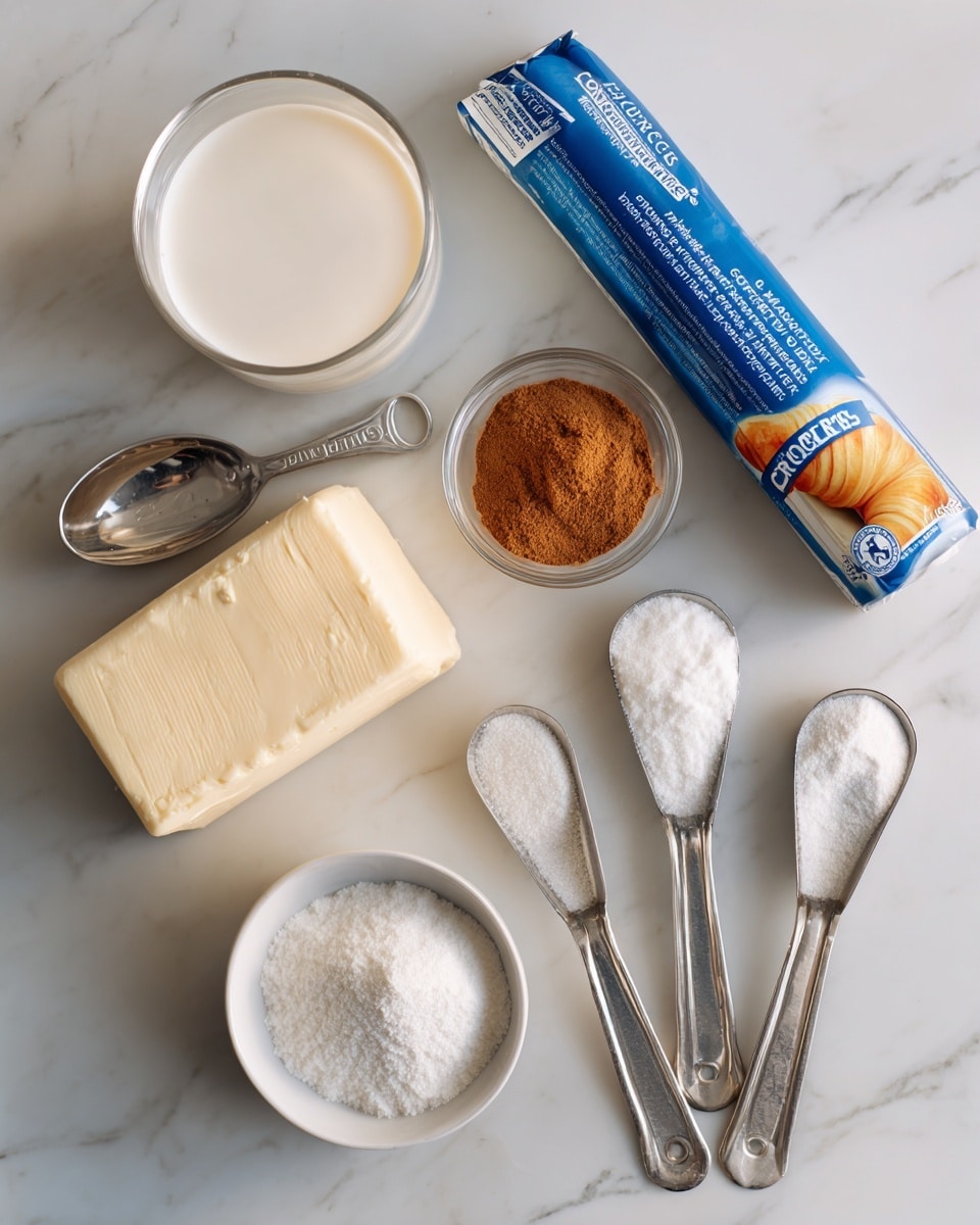 The image shows ingredients for baking with a white marbled surface as the base. In the center, there is a blue and yellow tube of crescent rolls. A small glass cup with light brown cinnamon powder and a silver measuring spoon is placed near the top center. To the left, a clear glass cup contains milk. Below it, a beige block of butter is positioned. On the right side, three hammered metal measuring spoons hold powdered sugar, white granulated sugar, and vanilla extract, which is in a small white bowl. Each ingredient is labeled with blue text nearby. photo taken with an iphone --ar 4:5 --v 7